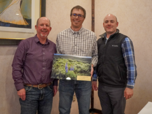 A photo of Kyle Tackett holding an award with Dave Smith to the left and Ron Leathers to the right.